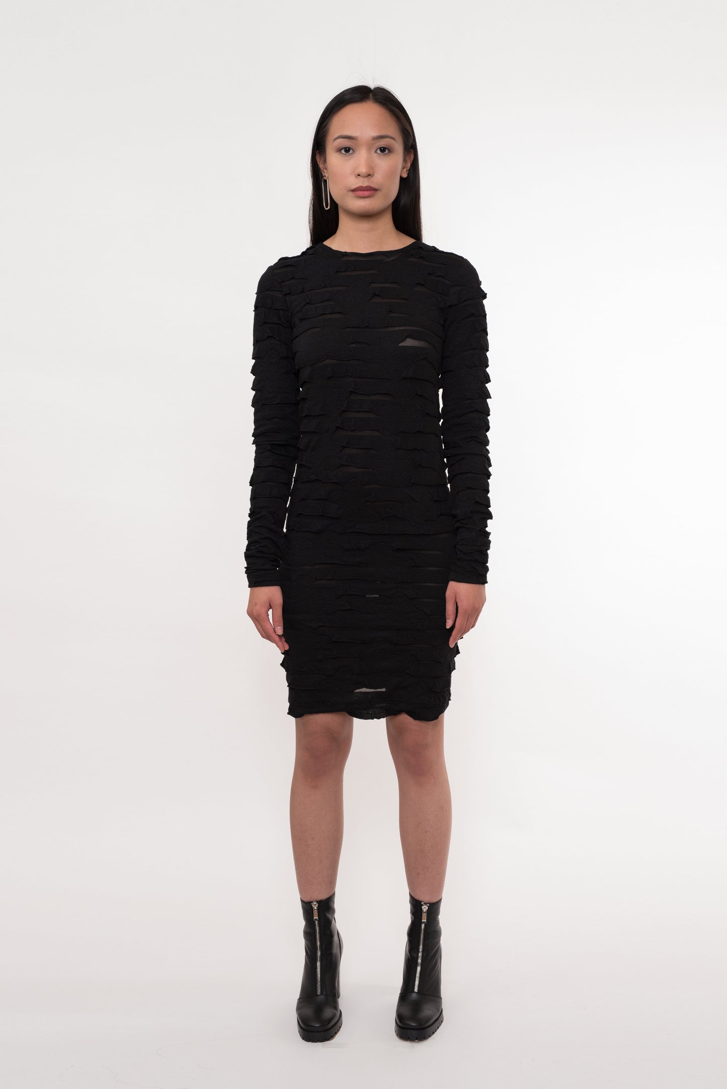 Model wearing long-sleeve black textured dress, facing forward with minimal background