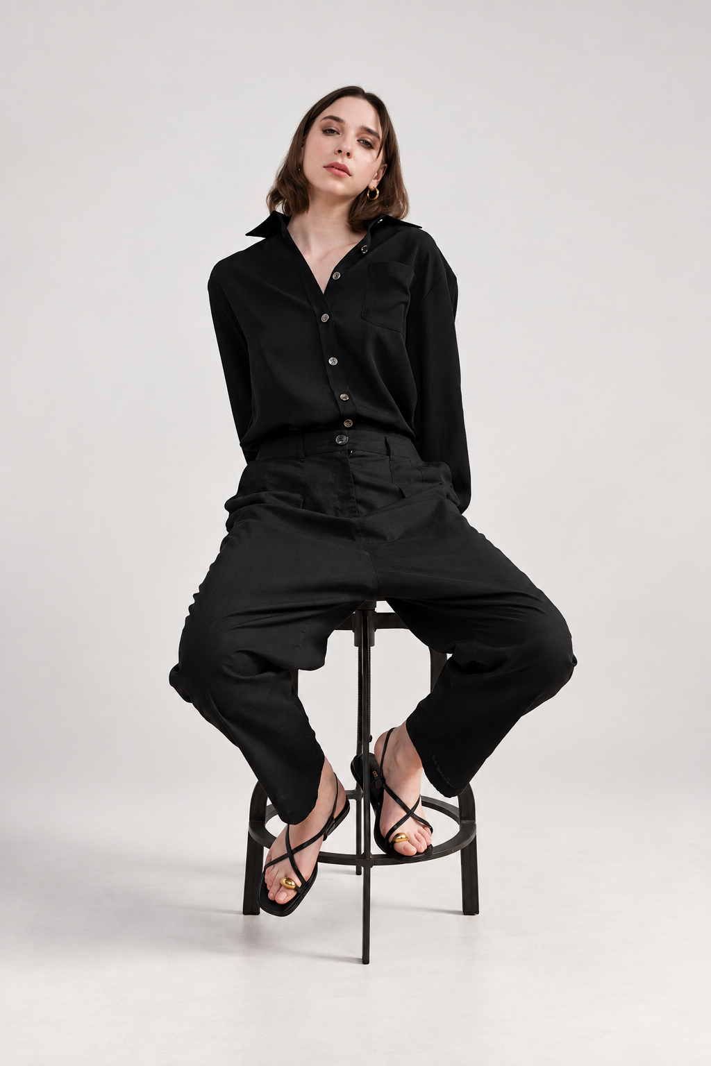 Model seated in Casa Como black relaxed trousers styled with a black long-sleeve shirt for a monochrome tailored look.