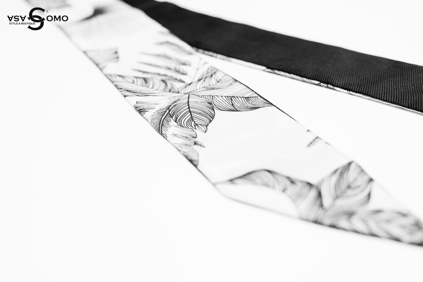 Close-up of a black and white silk twilly scarf showing fine tropical leaf detailing and smooth texture.