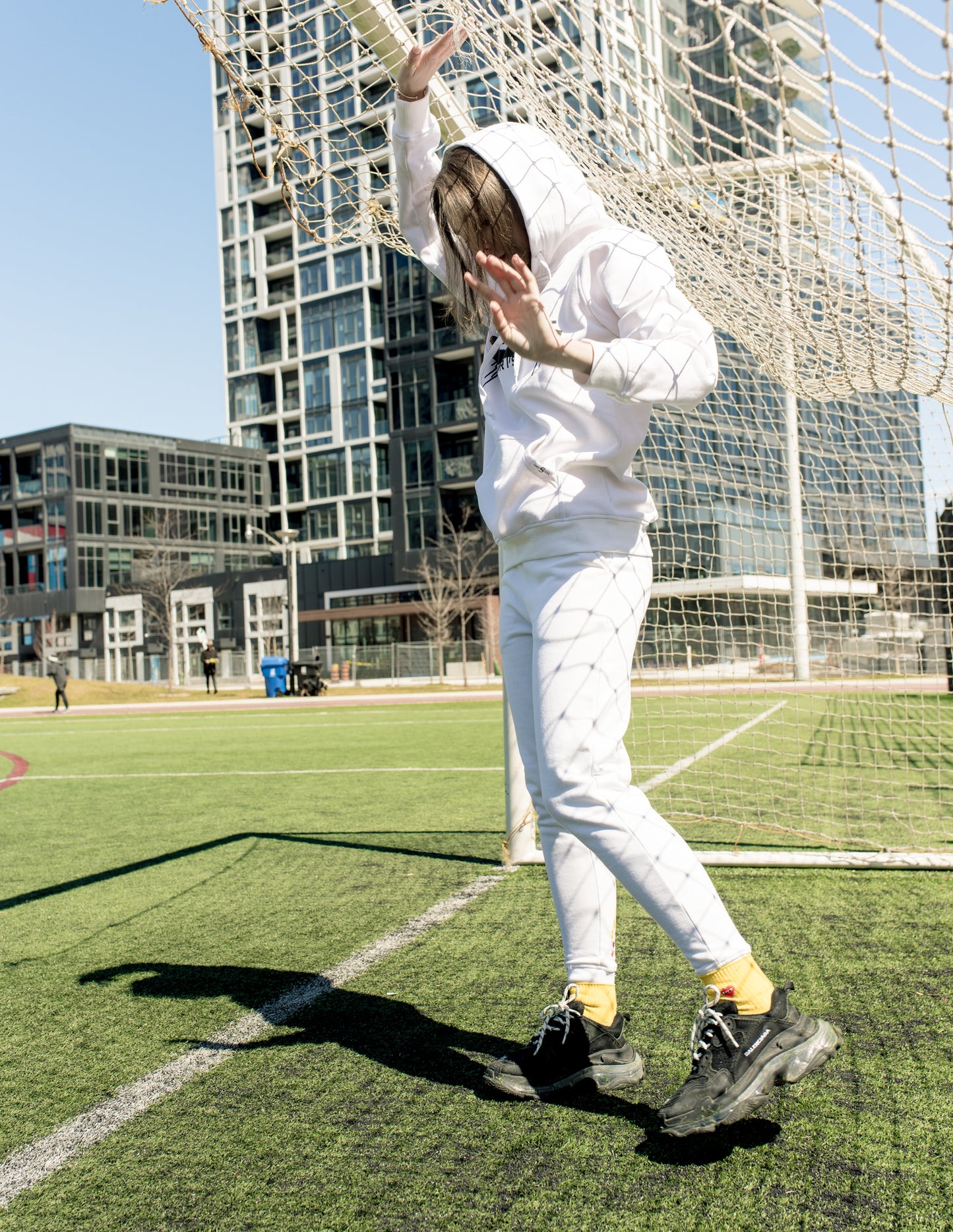 Woman wearing graphic white hoodie in soccer field setting – full body