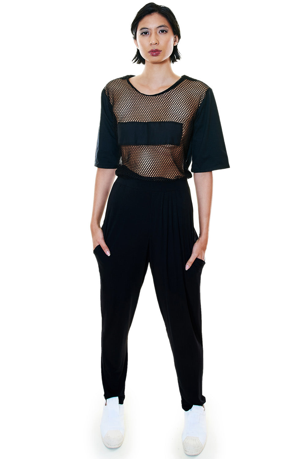 Woman wearing pleated black pants with mesh top – front view