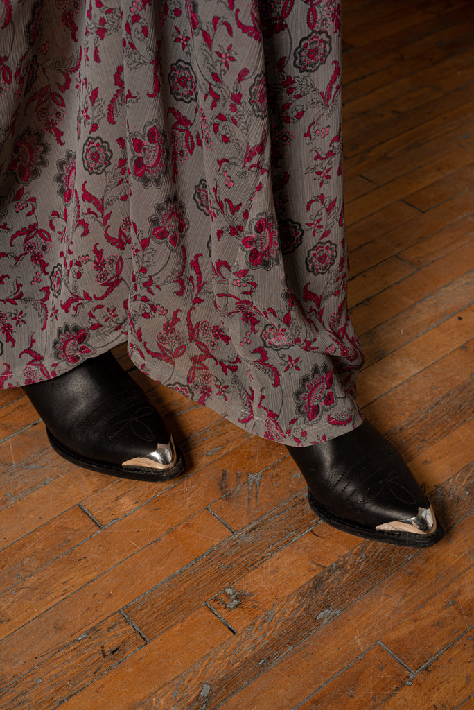 Close-up of black boots under a flowing gray floral chiffon dress with raspberry red print.