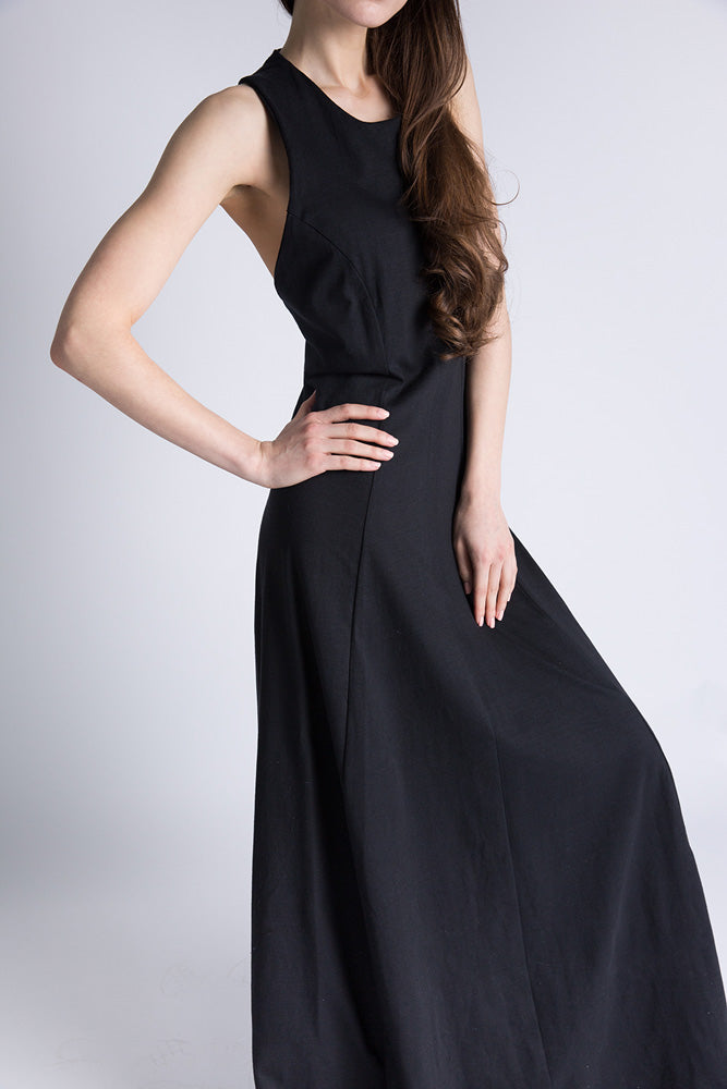 Model in a sleeveless black maxi dress with fitted bodice and flowing skirt, hands on hips.