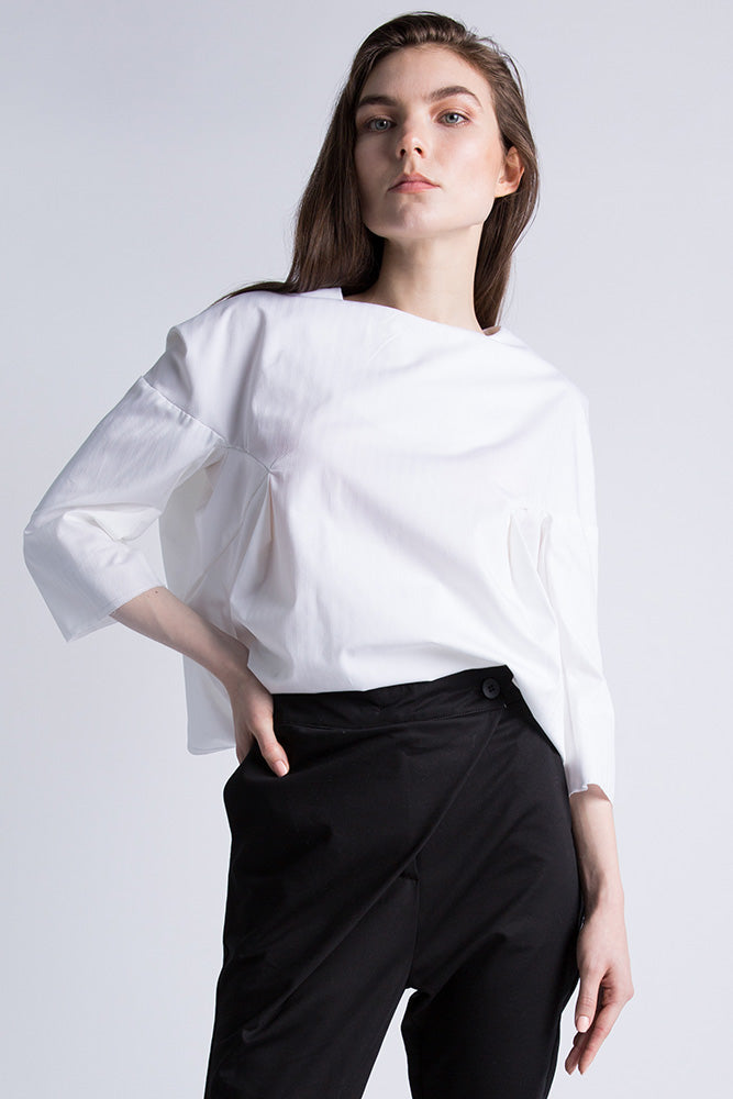 Model wearing white slit-back blouse with 3/4 sleeves, street-style setting