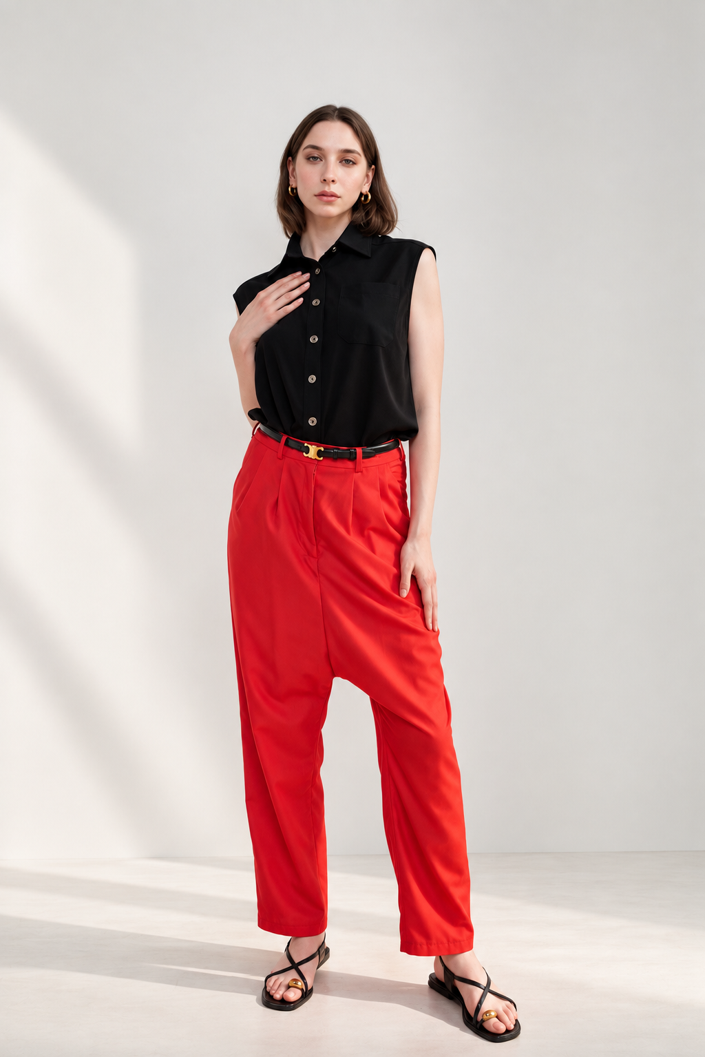 Model wearing Casa Como black sleeveless button-down blouse with red tailored pants, black belt and strappy sandals.