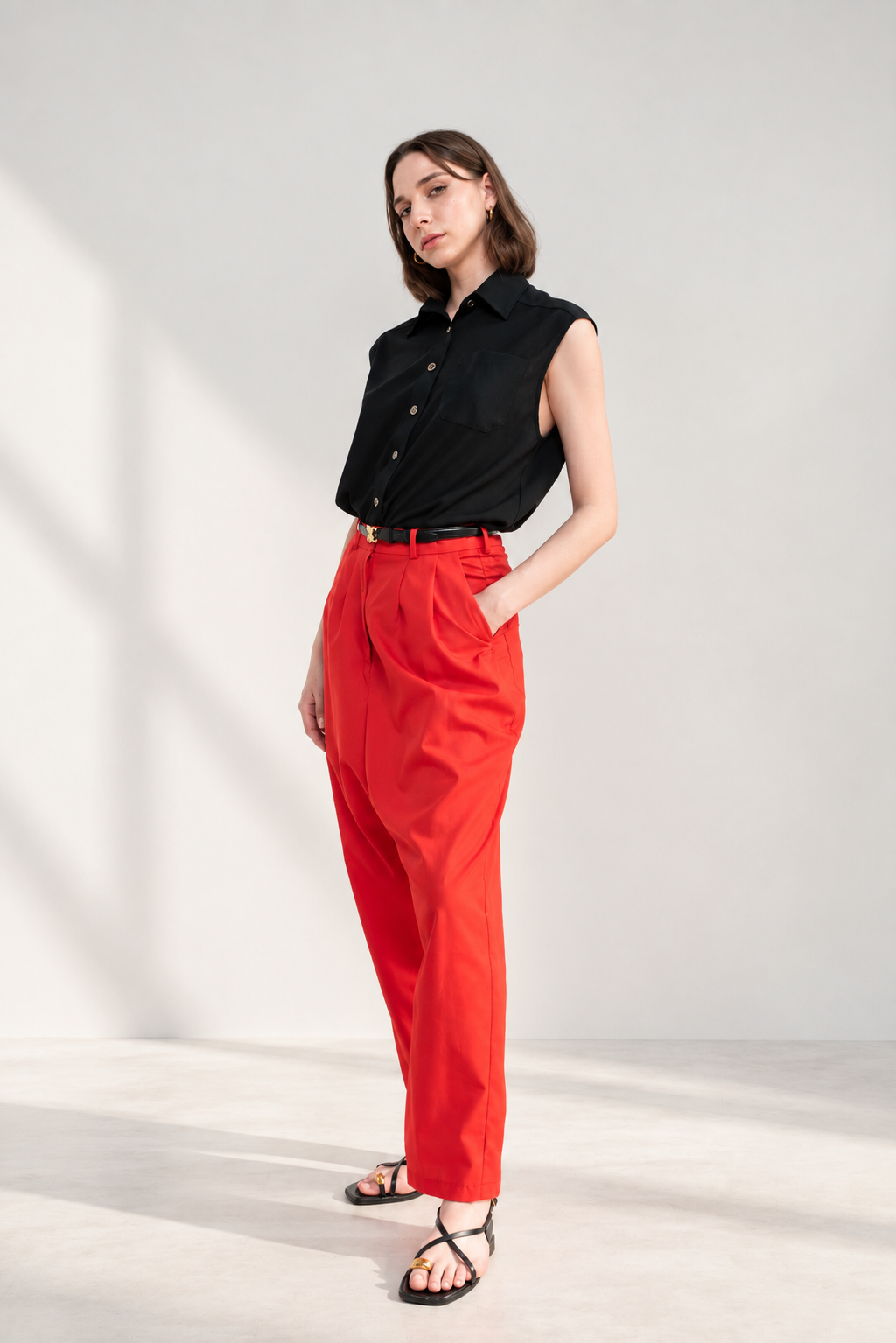 Model wearing Casa Como red tailored pants with a black sleeveless button-down blouse, black belt and strappy sandals.