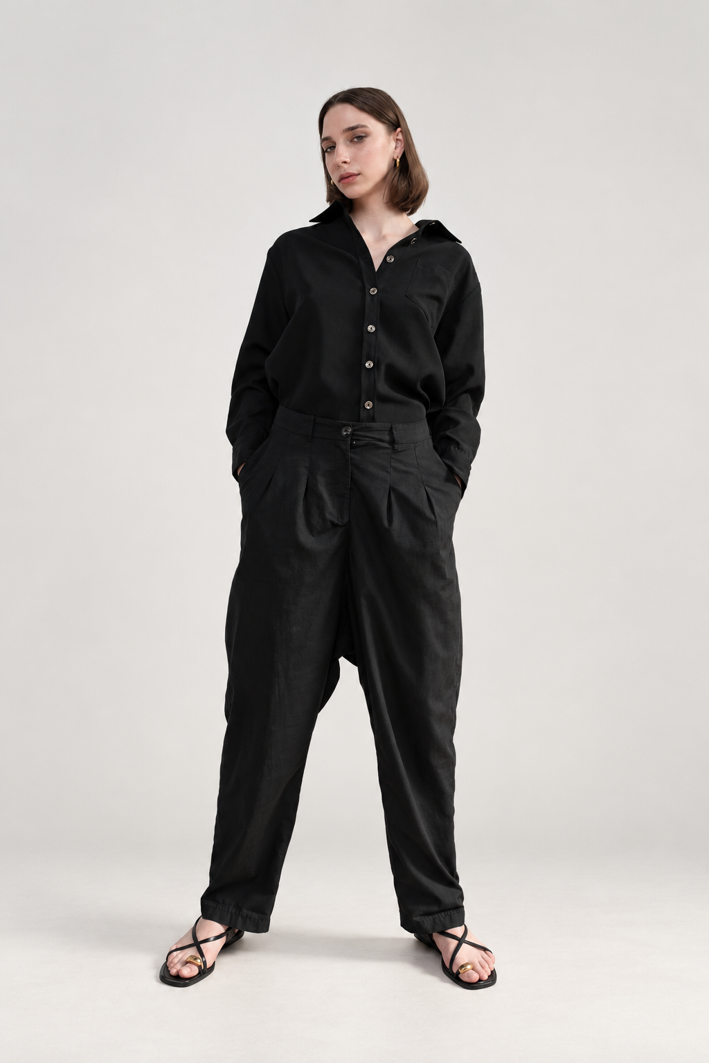 Model wearing Casa Como black relaxed pleated trousers with a black long-sleeve button-front shirt in a monochrome tailored look.