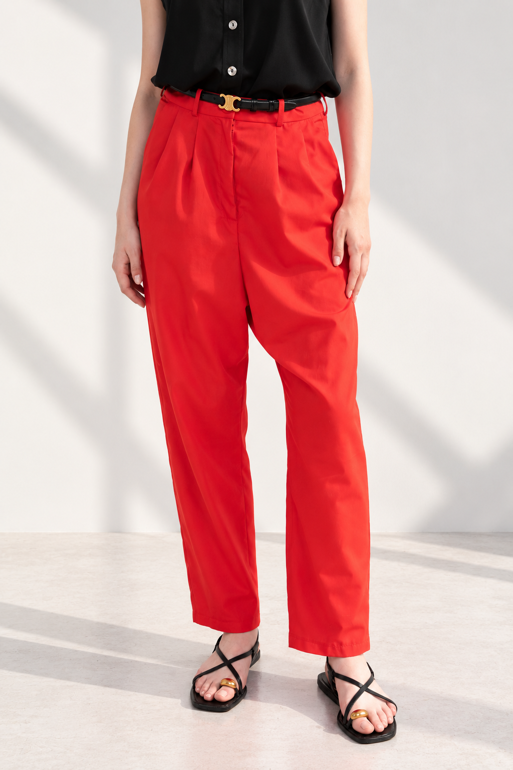 Casa Como red relaxed tailored trousers with pleated front, tapered leg and high-rise waist, styled with a black sleeveless blouse.