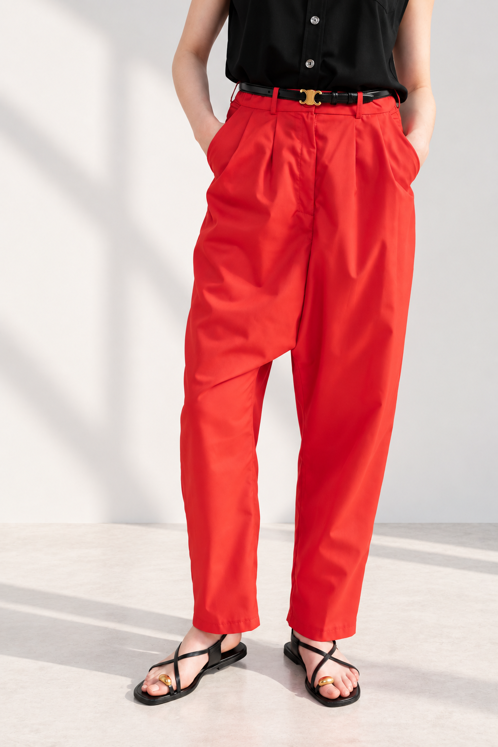 Model wearing Casa Como red high-waisted tailored trousers with pleated front, styled with a black sleeveless blouse and black sandals.