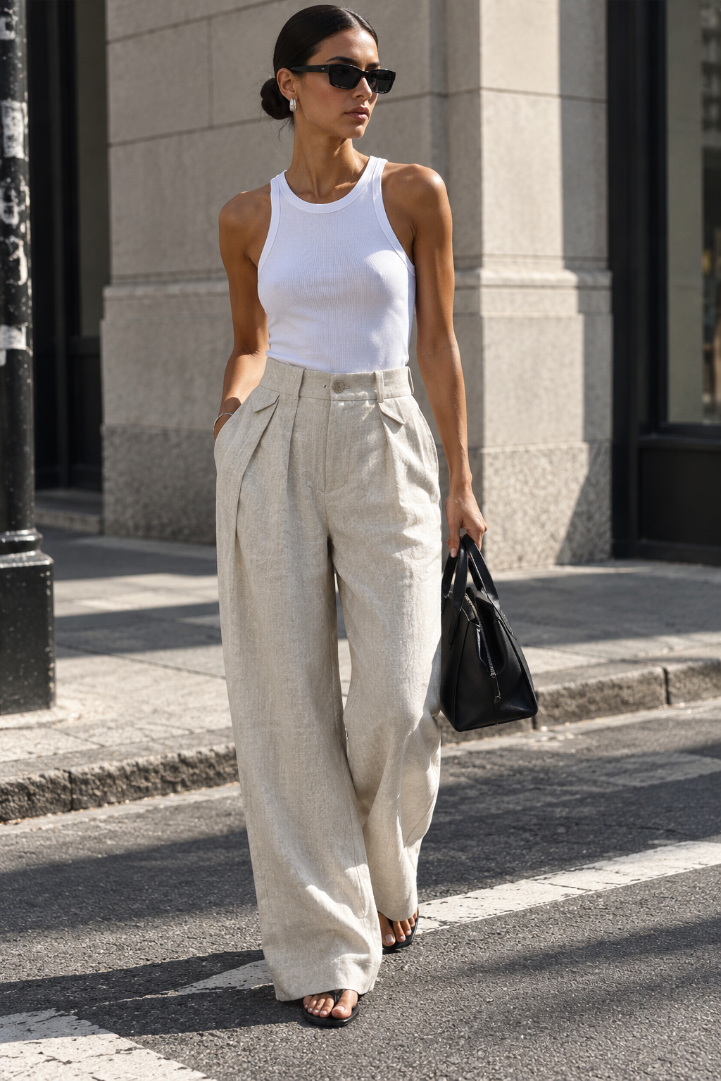 Model wearing Casa Como stone linen wide-leg trousers with a white fitted tank in an elevated city street-style look.