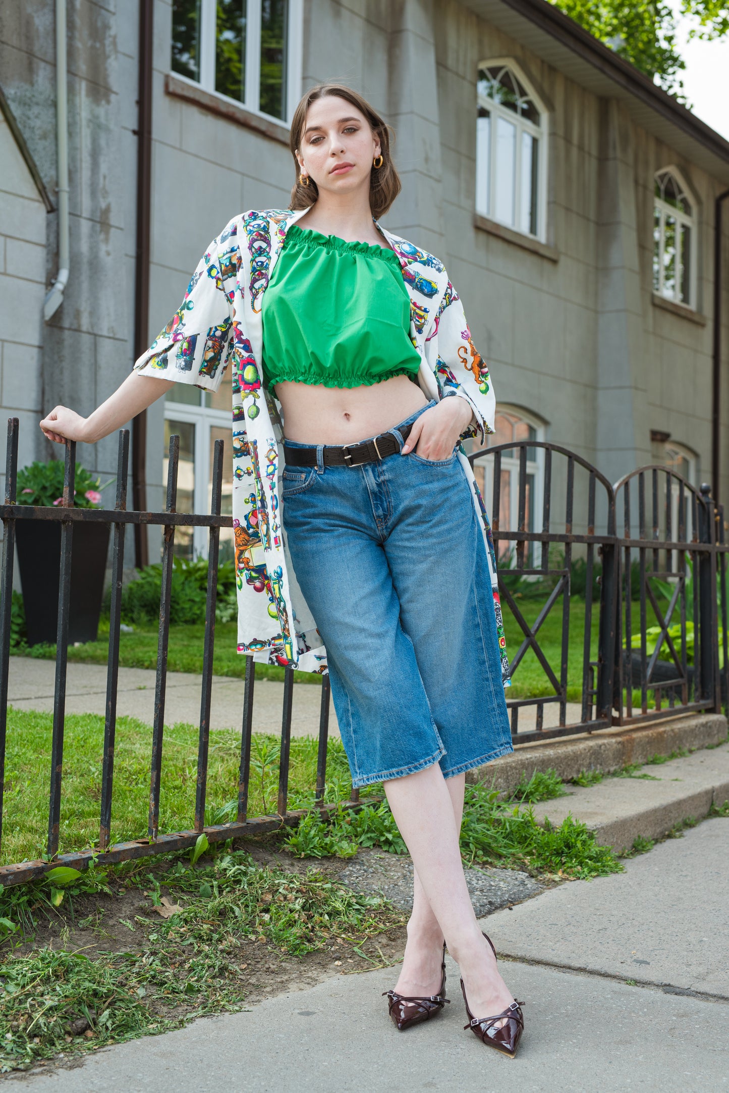 Woman wearing a floral kimono, green top, and blue jeans standing on a sidewalk.