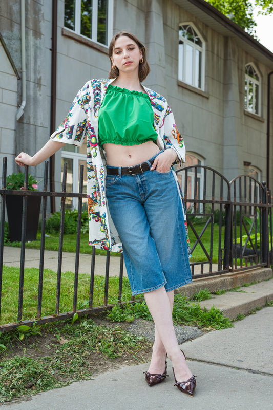 Woman wearing a floral kimono, green top, and blue jeans standing on a sidewalk.