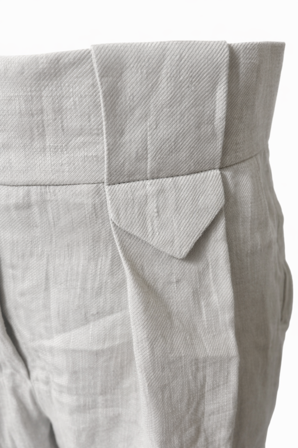 Close-up of stone linen trousers waistband and pocket flap detail showing textured natural fabric