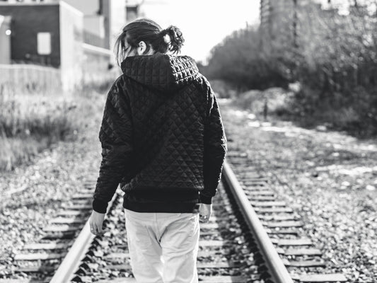 "Man wearing black quilted hoodie walking along train tracks – urban streetwear fashion